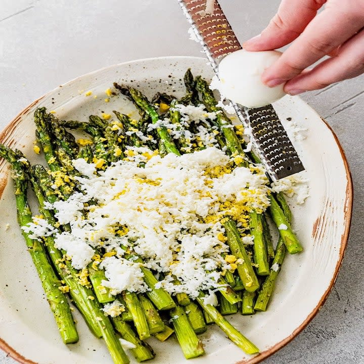 Grating an egg onto roasted asparagus.