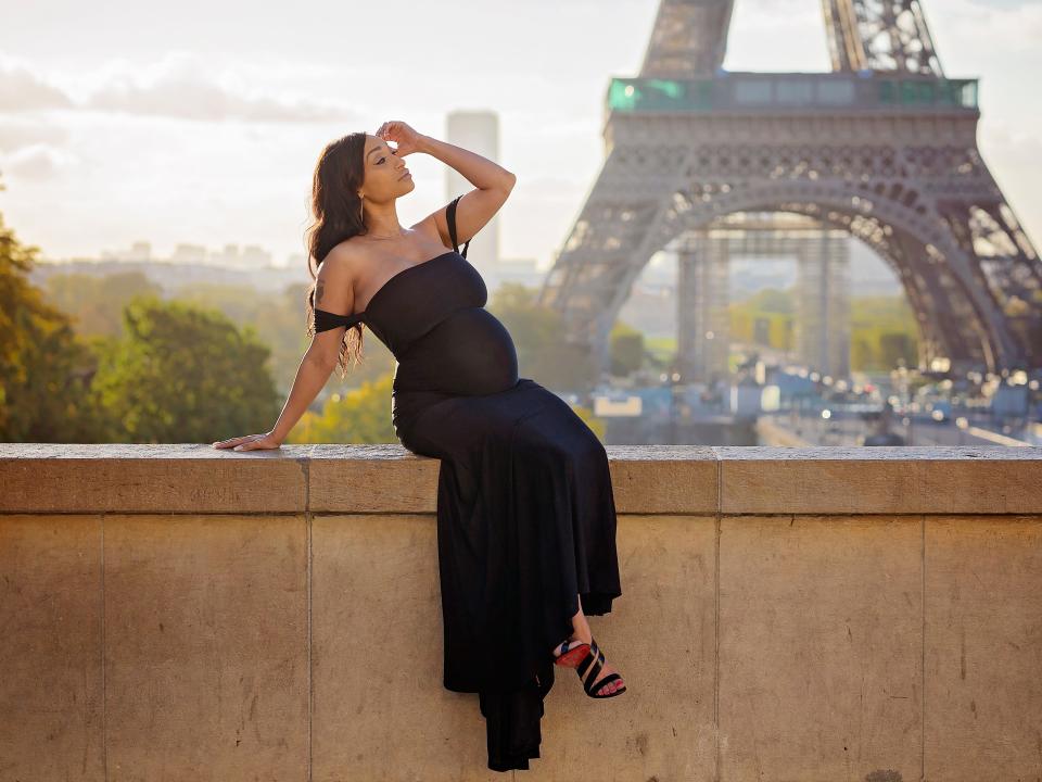 Andrea Alvarez, a mixed-race pregnant woman in a black gown, poses in front of the Eiffel Tower.
