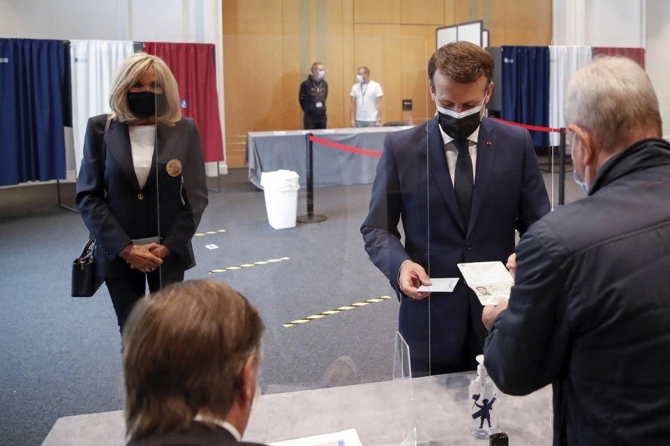 French President Emmanuel Macron shows his passport while his wife Brigitte waits during the first round of French regional and departmental elections, in Le Touquet-Paris-Plage, northern France, Sunday, June 20, 2021. The elections for leadership councils of France's 13 regions, from Brittany to Burgundy to the French Riviera, are primarily about local issues like transportation, schools and infrastructure. But leading politicians are using them as a platform to test ideas and win followers ahead of the April presidential election. (Christian Hartmann/Pool via AP)