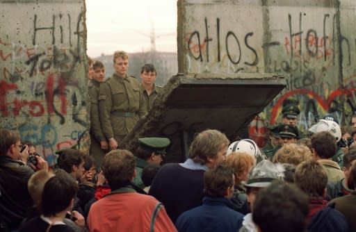 Berliners watch on November 11, 1989 as East German border guards demolish a section of the Berlin Wall, the biggest symbol of the Iron Curtain