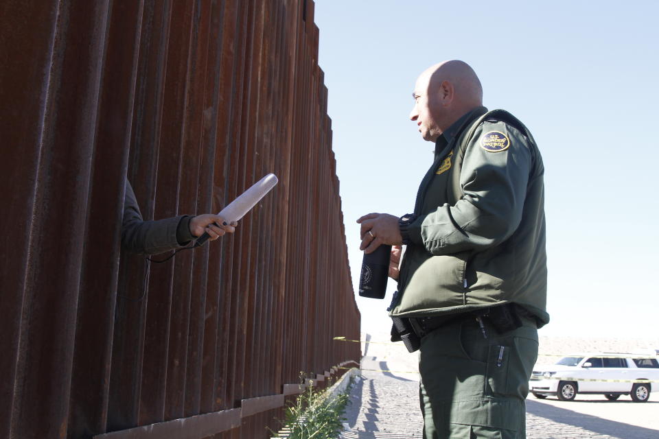 A journalist in Anapara, Mexico, sticks her microphone through a through a border fence to interview a Border Patrol agent following a training exercise on Friday, Jan. 31, 2020, in Sunland Park, New Mexico. Journalists in Mexico filmed the use-of-force exercises through gaps in the bollard-style wall. (AP Photo/Cedar Attanasio)