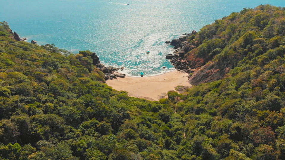 Beautiful secret beach Butterfly in Goa, India. Aerial view of pristine beach with rocky bay and waves crashing