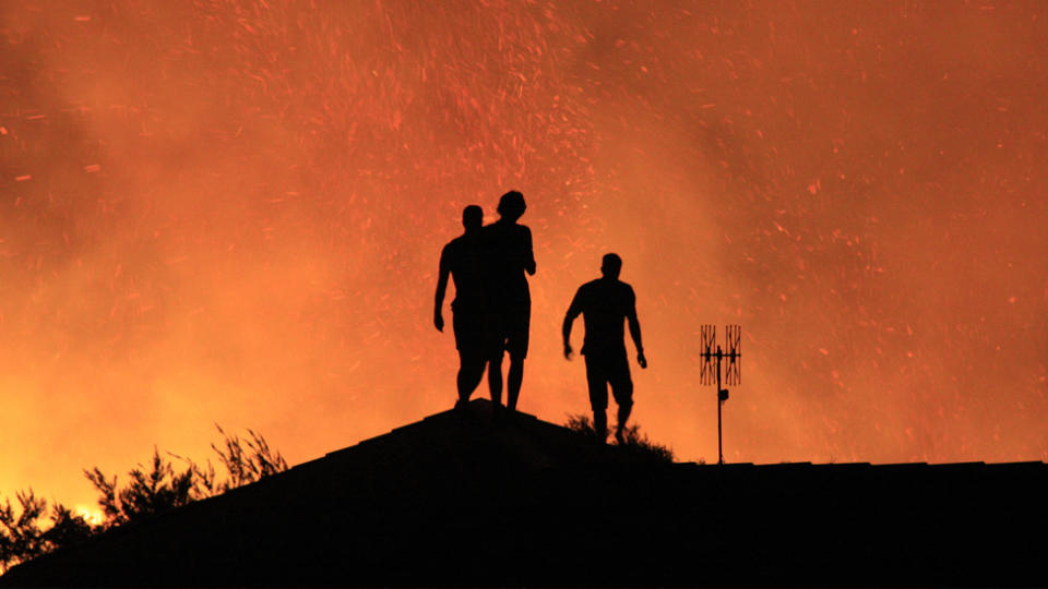 Residents pictured standing on their rooftop as bushfires rage at Sunshine Beach in the Noosa National park