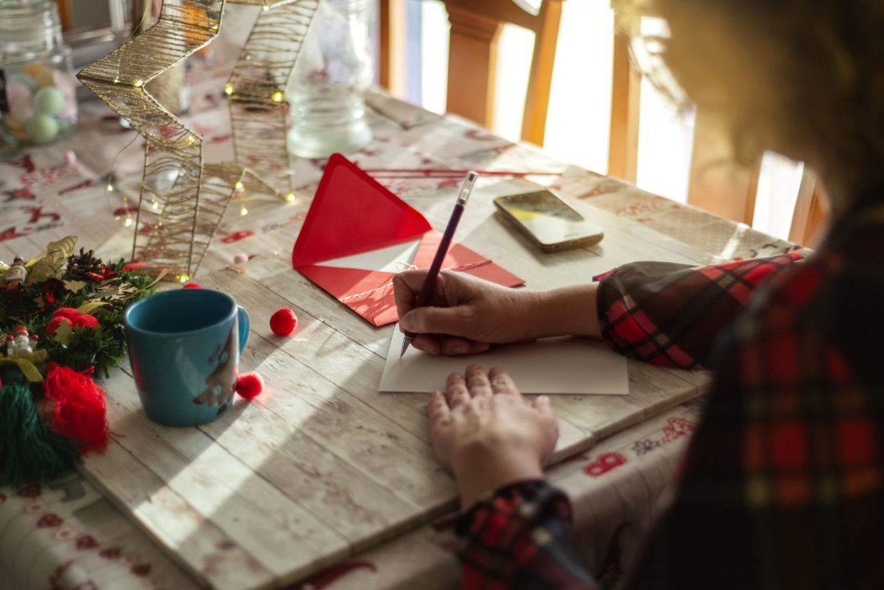 A woman writing a Christmas card on a wooden table