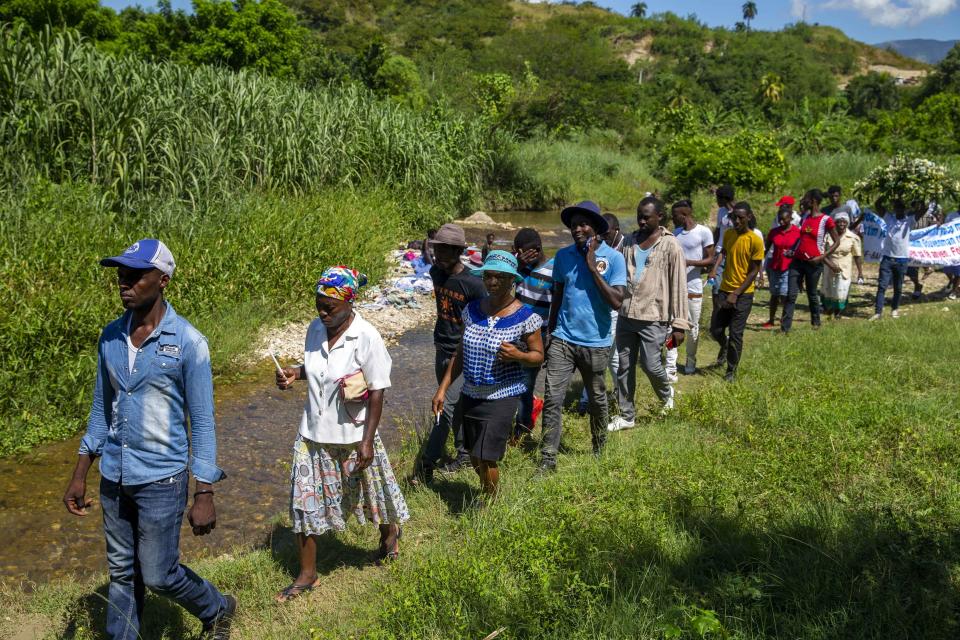 Cholera survivors walk along the Meille River to the former UN base where they will leave flowers as they commemorate 10 years since the cholera outbreak in Mirebalais, Haiti, Monday, Oct. 19, 2020. Ten years after a cholera epidemic swept through Haiti and killed thousands, families of victims still struggle financially and await compensation from the United Nations as many continue to drink from and bathe in a river that became ground zero for the waterborne disease. (AP Photo/Dieu Nalio Chery)
