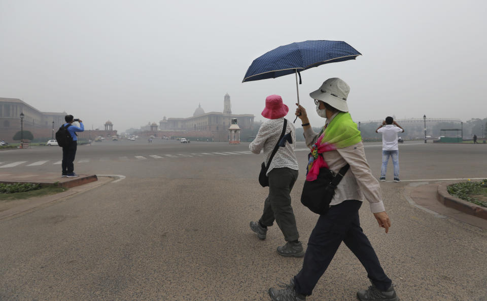 Foreign tourists wear pollution masks and walk at Raisna hills, enveloped by smog in New Delhi, India, Thursday, Nov. 7, 2019. The air quality index stood at 273 on Thursday in the capital after authorities declared a health emergency last weekend when the index crossed 500 — 10 times the level considered healthy by WHO standards. (AP Photo/Manish Swarup)