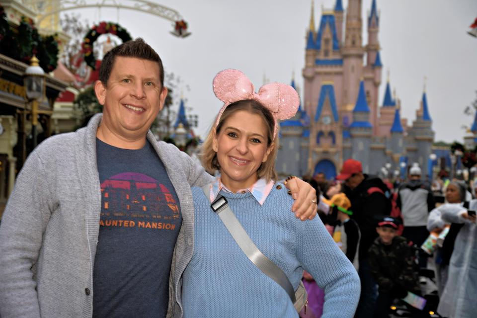terri and her husband posing for a photo in front of the castle at magic kingdom