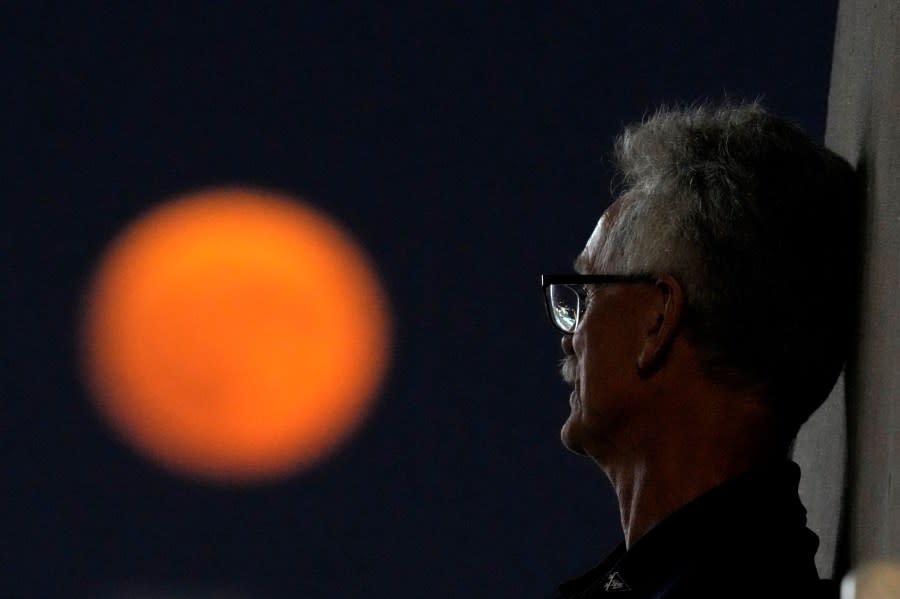 A man watches from the upper deck of a baseball game between the Kansas City Royals and the Pittsburgh Pirates as the moon rises in the distance Wednesday, Aug. 30, 2023, in Kansas City, Mo. The moon was a rare blue supermoon, named so because it was the second full moon in August, thus the blue label, and it was unusually close to Earth, therefore a supermoon. (AP Photo/Charlie Riedel)