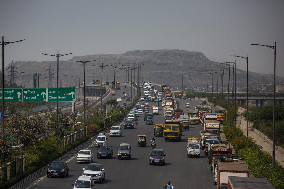 Traffic moves on a highway near the Bhalswa landfill on the outskirts of New Delhi, India, Wednesday, March 10, 2021. Every day, more than 2,300 tons of garbage is dumped at the landfill, which covers an area bigger than 50 football fields, with a pile taller than a 17-story building. And every day, thousands of scavengers climb the precarious slopes to pick through what can be salvaged. (AP Photo/Altaf Qadri)