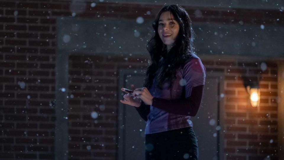 A still from Hawkeye shows Hailee Steinfeld as Kate Bishop standing on a roof wrapping her fingers