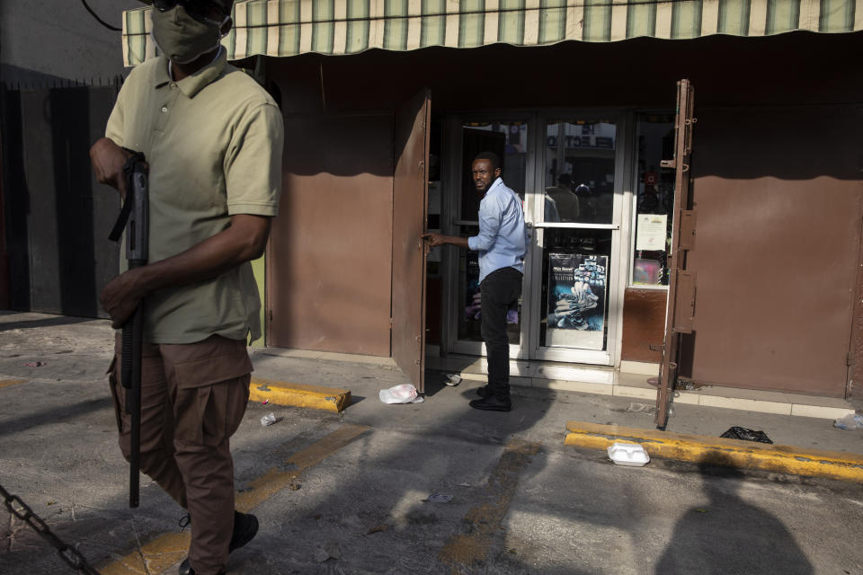 A private security guard stands watch as an employee opens up shop in the Petion-Ville neighborhood of Port-au-Prince, Haiti, early Monday morning, Sept. 27, 2021. For decades, the country was ruled by political strongmen supported by armed gangs; since the assassination of President Jovenel Moise, the state collapsed. (AP Photo/Rodrigo Abd)