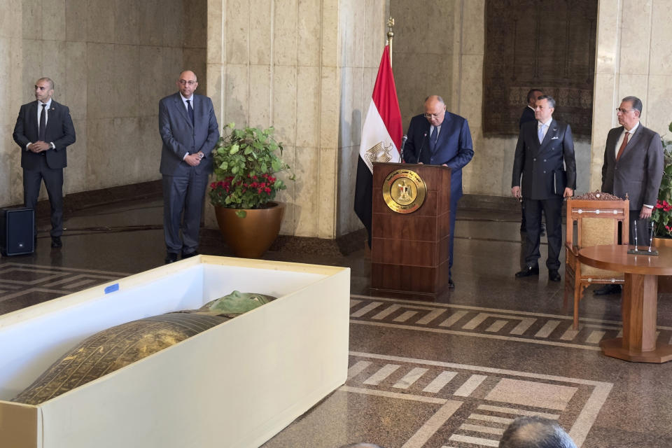 Foreign Minister Sameh Shoukry, center, standing in front of an ancient wooden sarcophagus, speaks during a handover ceremony at the foreign ministry in Cairo, Egypt, Monday, Jan. 2, 2023. An ancient wooden sarcophagus that was featured at the Houston Museum of Natural Sciences was returned to Egypt after U.S. authorities determined it was looted years ago, Egyptian officials said Monday. Tourism and Antiquities Minister Ahmed Issa, second right, listens. (AP Photo/Mohamed Salah)
