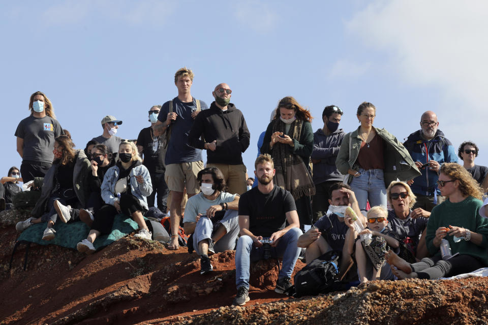 People gather on the top of a cliff to watch a tow surfing session at Praia do Norte or North Beach in Nazare, Portugal, Thursday, Oct. 29, 2020. A big swell generated earlier in the week by Hurricane Epsilon in the North Atlantic, reached the Portuguese west coast drawing big wave surfers to Nazare and thousands of spectators as well. (AP Photo/Pedro Rocha)