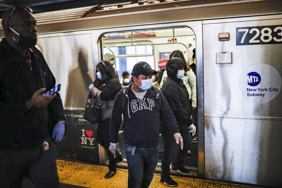 Subway riders, wearing personal protective equipment due to COVID-19 concerns, step off a train, Tuesday, April 7, 2020, in New York. The new coronavirus causes mild or moderate symptoms for most people, but for some, especially older adults and people with existing health problems, it can cause more severe illness or death. (AP Photo/John Minchillo)