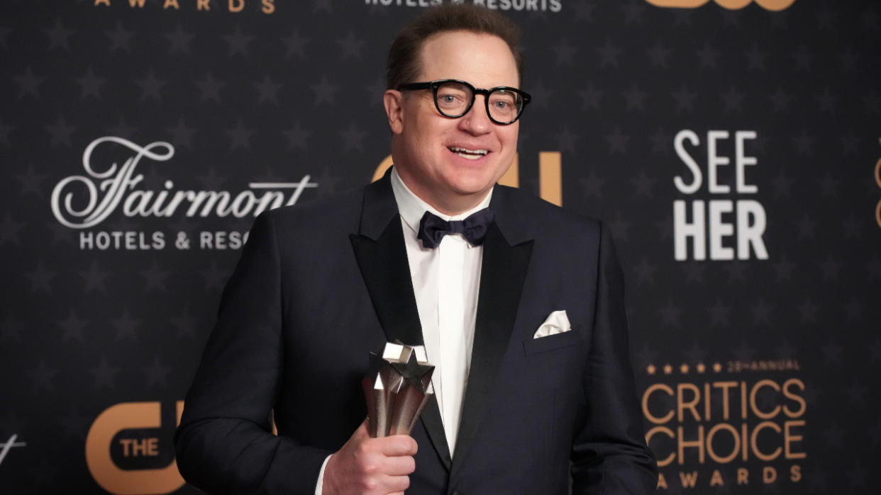  Brendan Fraser stands dressed in a black tuxedo, holding his Critic's Choice Award.  