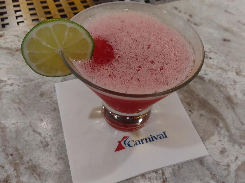 A pink cocktail with a lime on the edge on a Carnival Cruise Line branded napkin.
