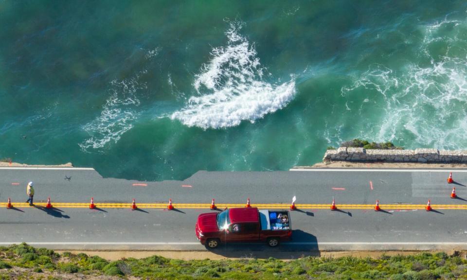 A car on a damaged road next to a cliff.