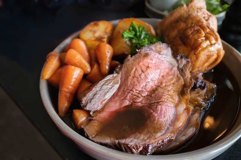 Roast beef slices on a plate with carrots, roast potatoes, a Yorkshire pudding and gravy, making a complete Sunday roast meal.