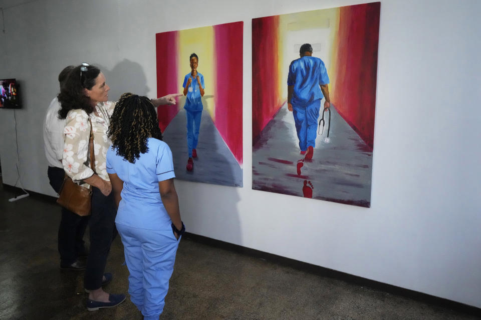 Zimbabwean artist and nurse Deodoris Mawanda, right, stands in front of her paintings, in Harare, Wednesday, March 8, 2023. Mawanda is one of 21 female artists whose works have been on show at the southern African country's national gallery since International Women's Day on March 8. The exhibition is titled "We Should All Be Human" and is a homage to women's ambitions and their victories, art curator Fadzai Muchemwa said. (AP Photo/Tsvangirayi Mukwazhi)