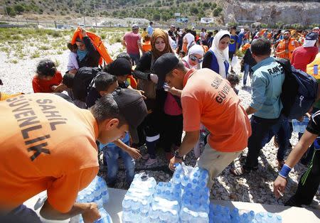 Turkish coast guards offer bottles of water to Syrian migrants on the shore in Cesme, near the Aegean port city of Izmir, Turkey, August 11, 2015. REUTERS/Osman Orsal