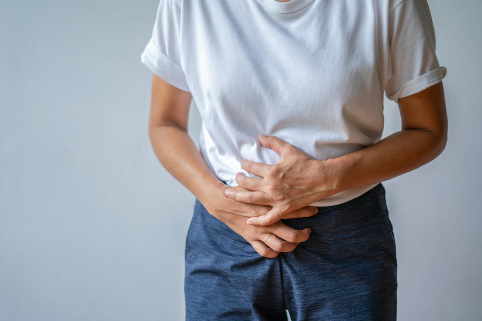 A young woman holding her lower abdomen, in pain due to cramps or a stomachache.