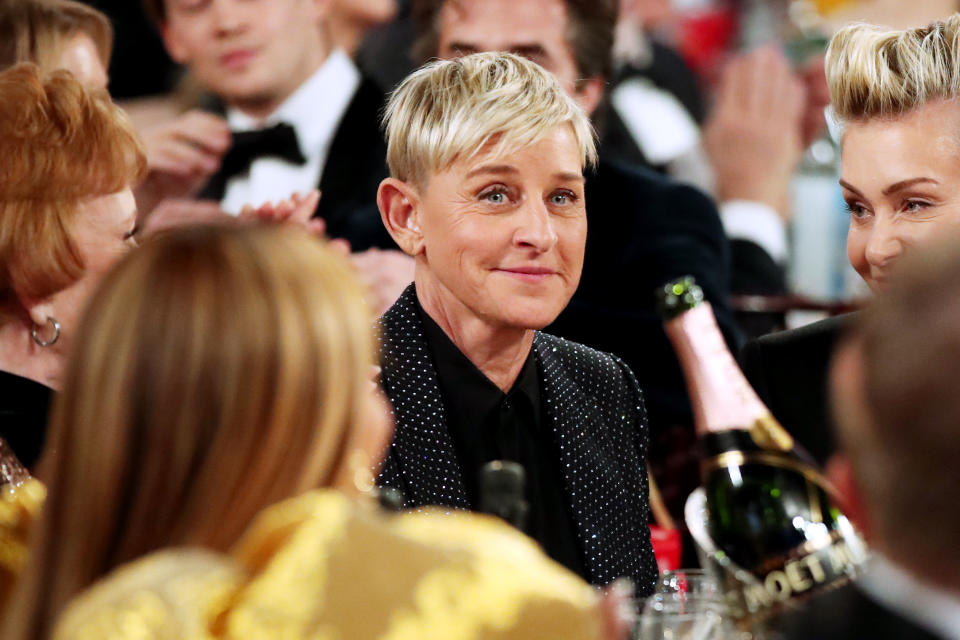 Ellen DeGeneres in a dotted suit at an event, surrounded by guests and champagne