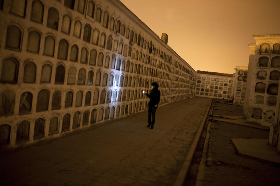 In this Dec. 6, 2012 photo, a woman examines niches with a flashlight as she takes a nighttime guided tour through the Presbitero Matias Maestro cemetery in Lima, Peru. There are no more burials anymore, unless a family owns a mausoleum. (AP Photo/Rodrigo Abd)