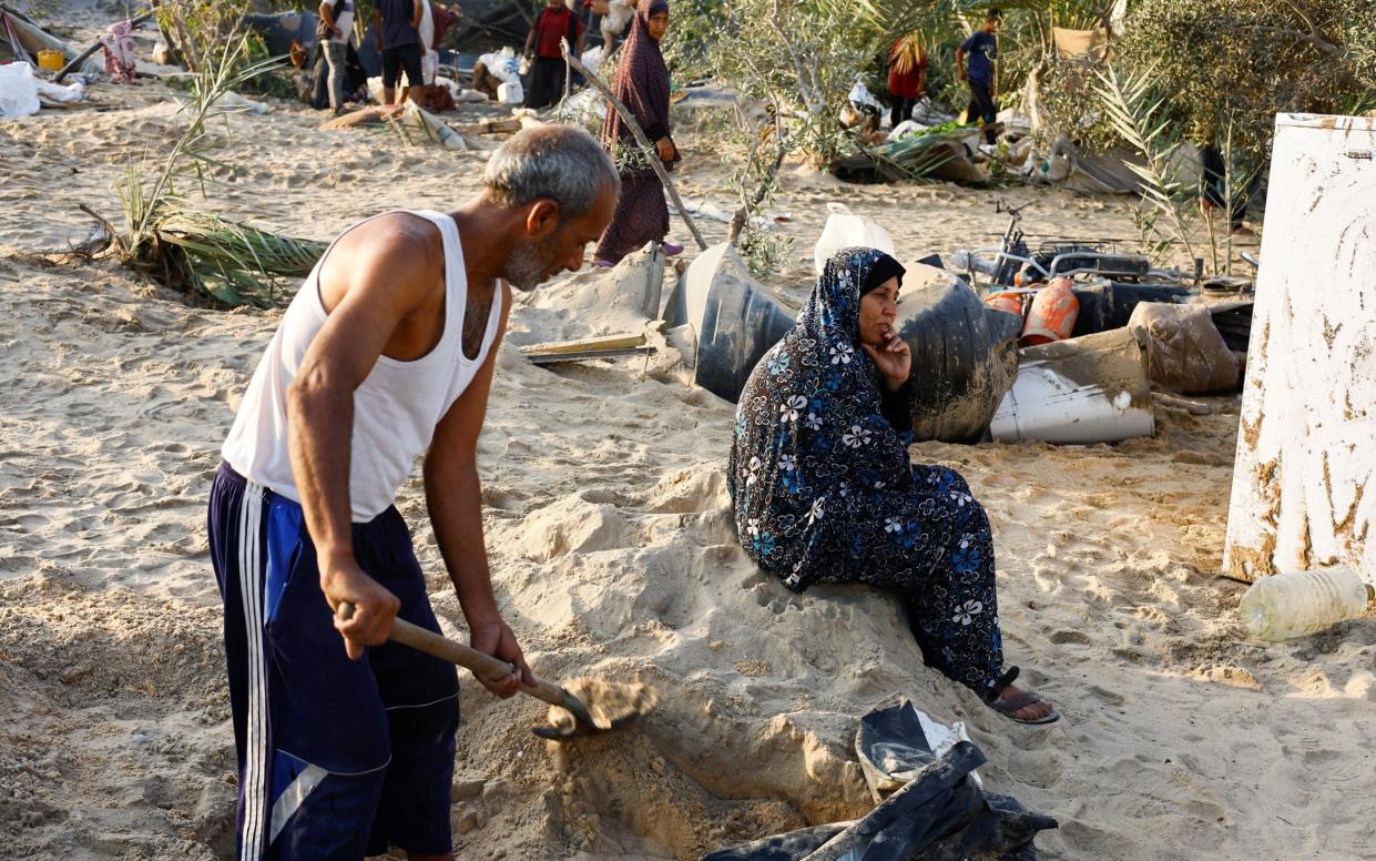 A Palestinian man is seen digging in the sand following Israel's overnight airstrike on a tent camp in Khan Younis