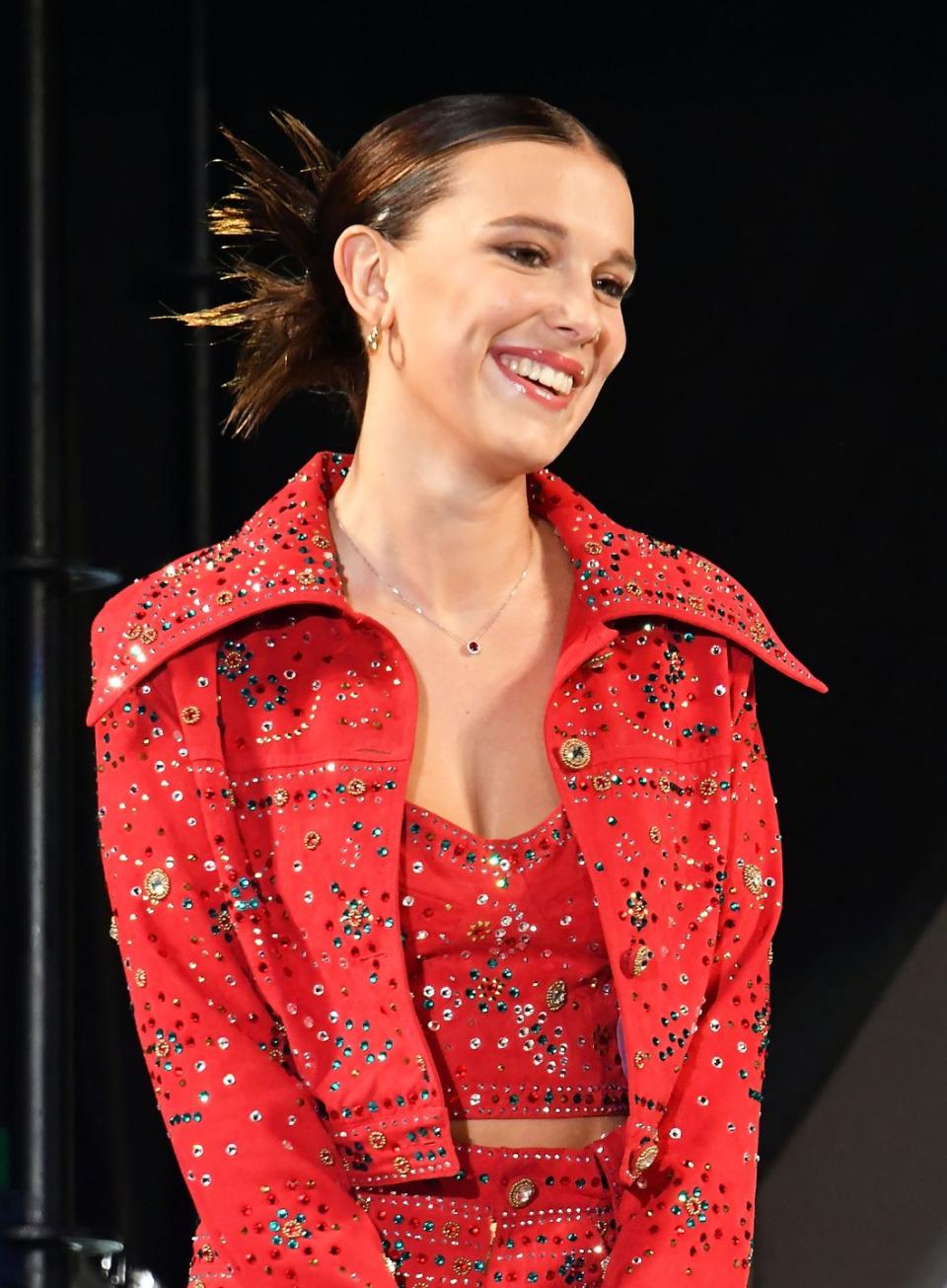 millie bobby brown wearing a bejewelled red crop jacket matching bustier bra top and high rise hot pants