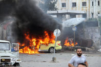 Syrians gather near a burning car at the scene of one of the suicide bombings in the coastal town of Tartus, Syria, on May 23, 2016. (SANA via AP)