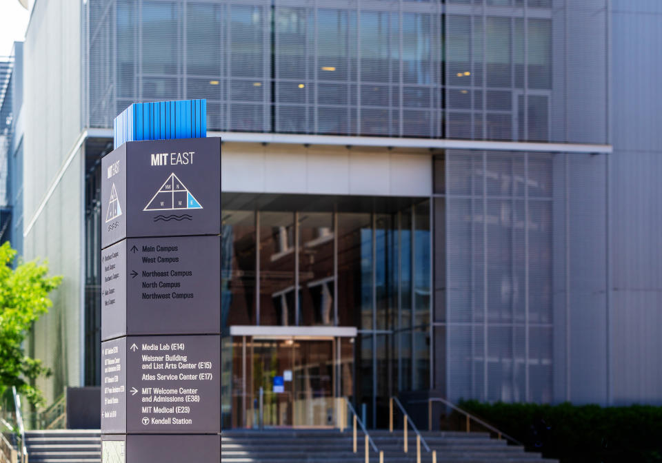 Cambridge, Massachusetts, USA - June 30, 2022:  A directional sign post with arrows pointing to various buildings on MIT's East campus. The MIT Media Lab building is in the background.