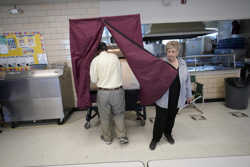 Precinct commissioner Mary Ann Winningkoff holds open a curtain of a voting booth as people vote at a polling place at St. Rita's Catholic School on election day in Harahan, La., Saturday, Oct. 14, 2023. (AP Photo/Gerald Herbert)