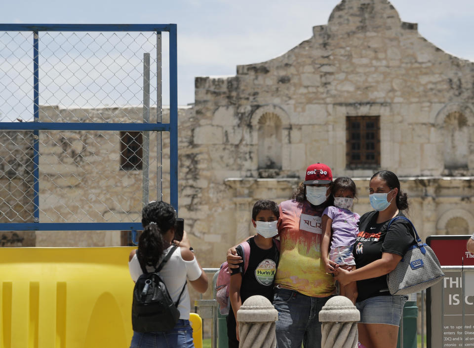 Visitors wearing masks to protect against the spread of COVID-19 pose for photos at the Alamo, which remains closed, in San Antonio, Wednesday, June 24, 2020. Cases of COVID-19 have spiked in Texas and the governor of Texas is encouraging people to wear masks in public and stay home if possible. (AP Photo/Eric Gay)