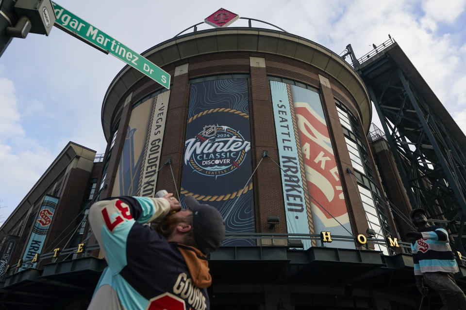 A fan wearing a Seattle Kraken center Yanni Gourde jersey drinks a beer outside of T-Mobile Park signs for the NHL Winter Classic hockey game between the Seattle Kraken and the Vegas Golden Knights, Monday, Jan. 1, 2024, in Seattle. (AP Photo/Lindsey Wasson)