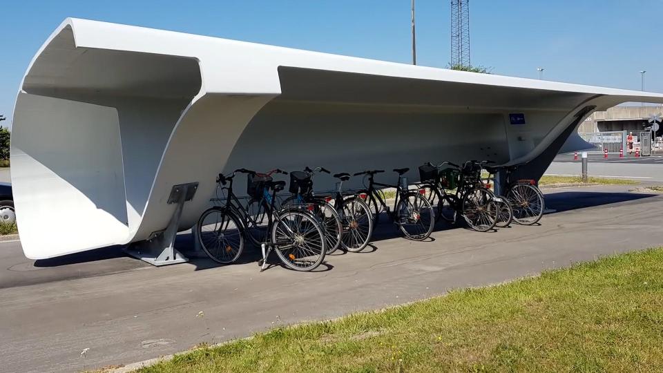A section of a wind turbine provides shade a rack full of bikes.