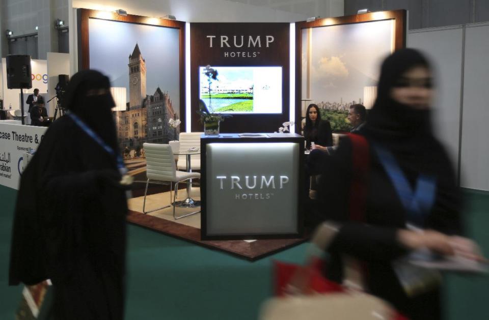 FILE- In this Tuesday, April 26, 2016 file photo, Arab women walk past the Trump Hotels stand at the Arabian Travel Market exhibition in Dubai, United Arab Emirates. Just two days after banning travelers from seven Muslim-majority nations, U.S. President Donald Trump invited the Saudi monarch, whose kingdom includes Islam’s holiest sites, to fly to Washington. It points to the delicate balancing act Trump faces as he tries to deliver on campaign promises to exterminate “radical Islamic terrorism” without endangering political and economic ties with U.S. allies in the region, many of which are countries where the Trump Organization has business interests. (AP Photo/Kamran Jebreili, File)