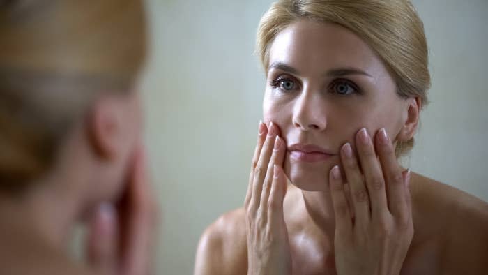 Disappointed woman looking at face reflection in mirror