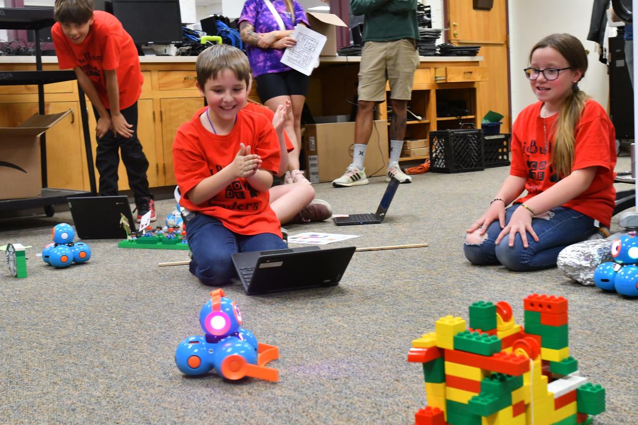 Irving Elementary School fourth grader Mason Durbin celebrates with his classmates after successfully coding a skit with a small blue Dash robot.