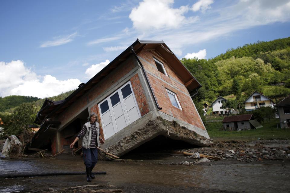 A woman reacts as she walks near a house tilted by floods in the village of Krupanj, west from Belgrade