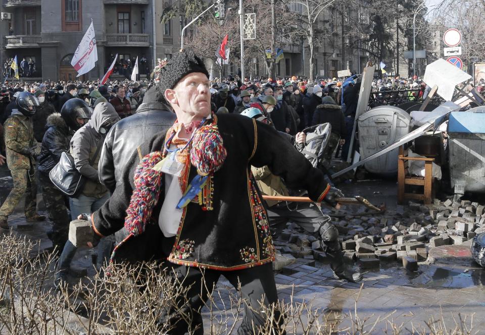 An anti-government protester dressed in Ukrainian national dress throws a stone during clashes with riot police outside Ukraine's parliament in Kiev, Ukraine, Tuesday, Feb. 18, 2014. Some thousands of anti-government protesters clashed with police in a new eruption of violence Tuesday. (AP Photo/Efrem Lukatsky)