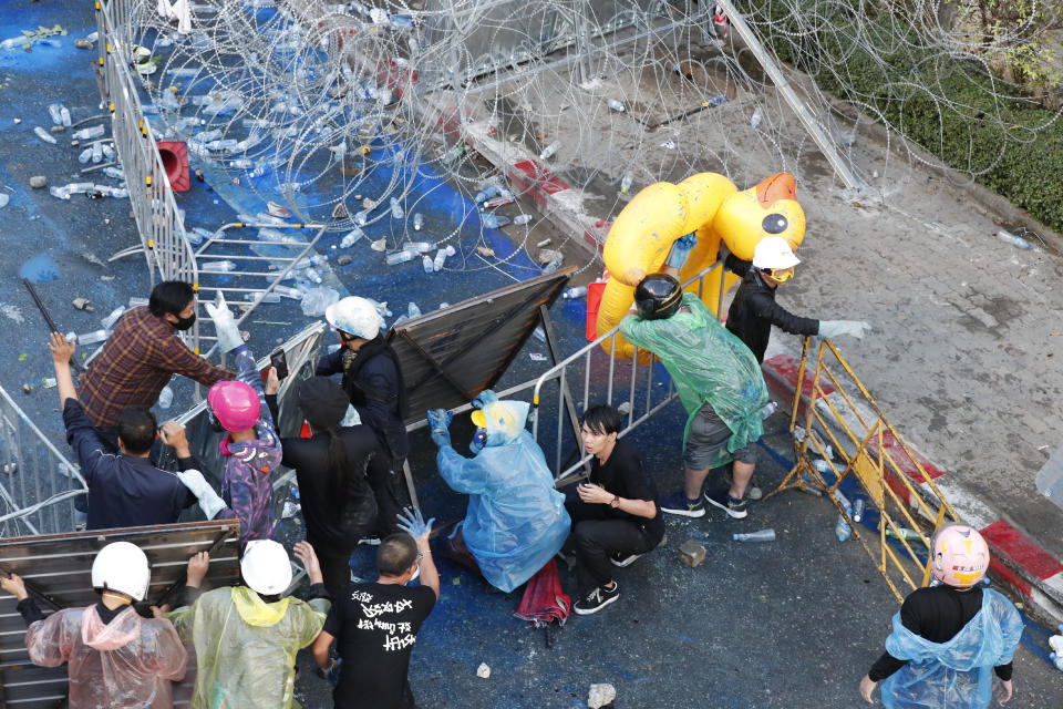 Democracy protesters take cover after breaking through a barricade during an anti-government rally near the Parliament in Bangkok, Tuesday, Nov. 17, 2020. Thailand's political battleground shifted to the country's Parliament Tuesday, where lawmakers are considering proposals to amend the country's constitution, one of the core demands of the student-led pro-democracy movement. (AP Photo/Sakchai Lalit)