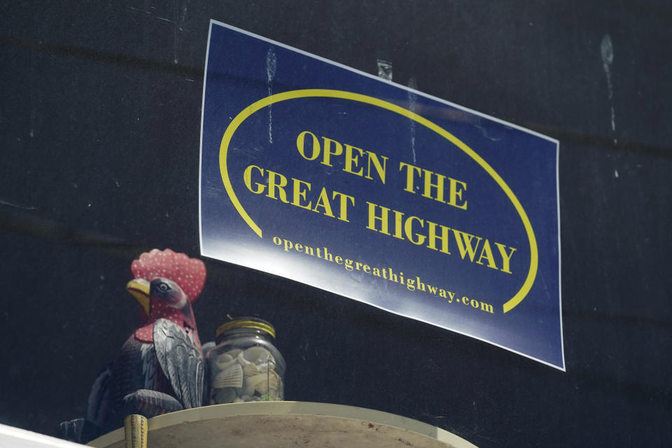 A sign hangs in the window of a home overlooking the car-free Great Highway in San Francisco, on Wednesday, April 28, 2021. At the start of the pandemic, San Francisco closed off parts of a major beachfront highway and Golden Gate Park to cars so that people had a safe place to run and ride bikes. Open space advocates want to keep those areas car-free as part of a bold reimagining of how U.S. cities look. But opponents decry the continued closures as elitist, unsafe and nonsensical now that the pandemic is over and people need to drive again. (AP Photo/Eric Risberg)