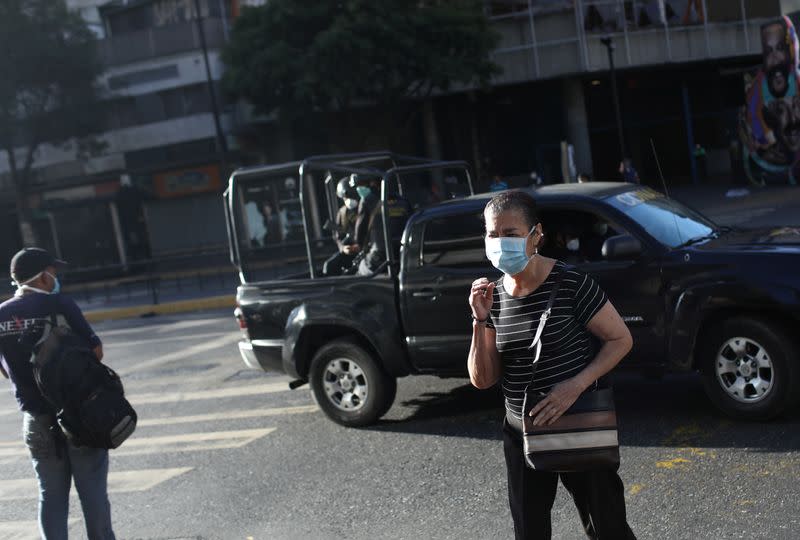 People wearing masks on the streets while a National Police vehicle passes by after the start of quarantine in Caracas