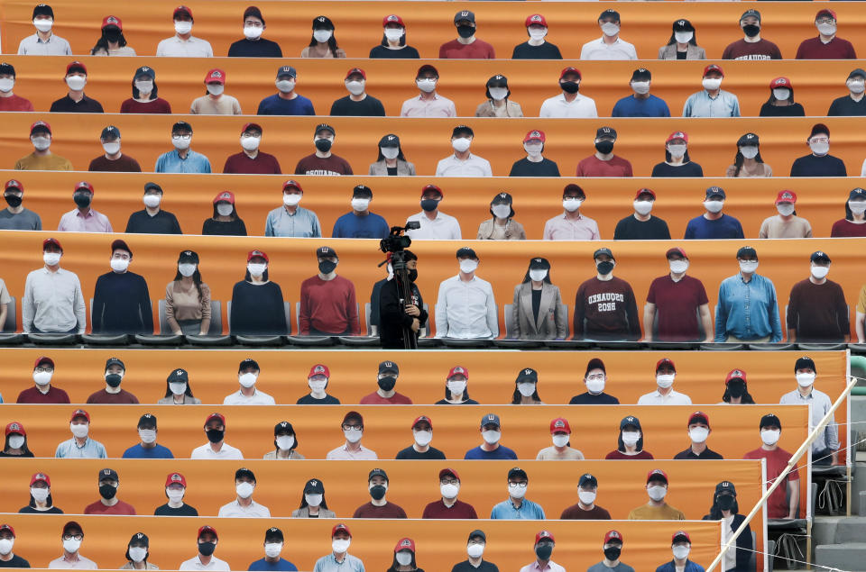 A TV cameraman walks through the spectators' seats which are covered with pictures of fans, before the start of a regular season baseball game between Hanwha Eagles and SK Wyverns in Incheon, South Korea, Tuesday, May 5, 2020. South Korea's professional baseball league start its new season on May 5, initially without fans, following a postponement over the coronavirus. (AP Photo/Lee Jin-man)