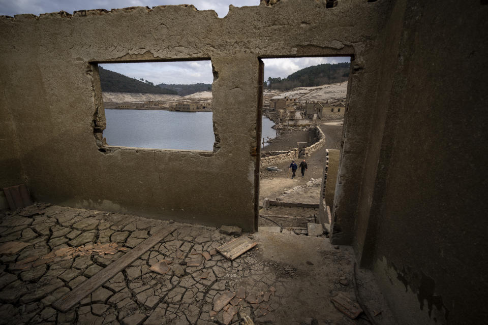 Jose Penin, 72, walks with his brother Julio, 78, as they visit the old village of Aceredo emerged due to drought at the Lindoso reservoir, in northwestern Spain, Friday, Feb. 11, 2022. Roofs emerging from the waters have become a common scene every summer at the Lindoso reservoir, in northwestern Spain. In especially dry years, parts of the old village of Aceredo, submerged three decades ago when a hydropower dam flooded the valley, would appear. But never before had the skeleton of the village emerged in its entirety, in the middle of the usually wet winter season. (AP Photo/Emilio Morenatti)