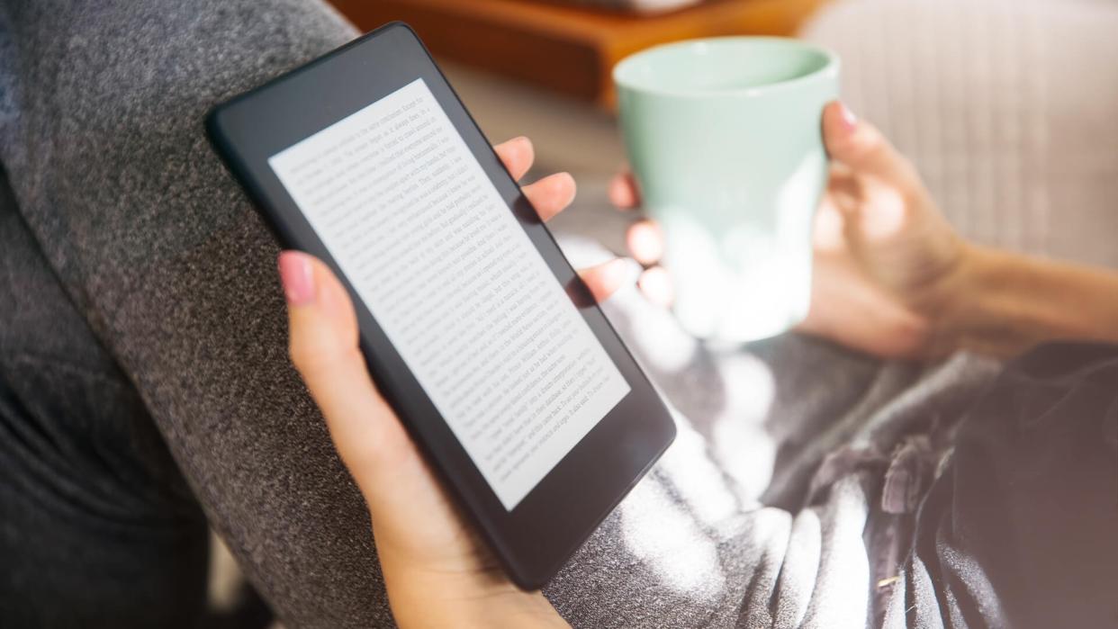 Young woman drinking coffee and using an ebook reader in the sofa.