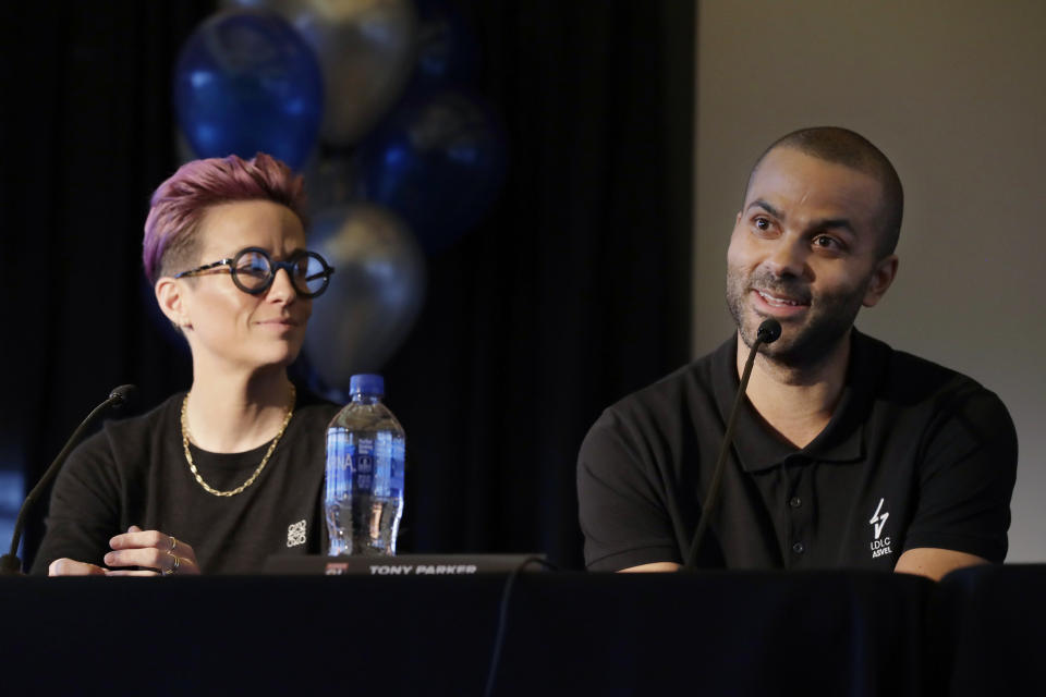 Megan Rapinoe, left, a forward with the National Women's Soccer League's Reign FC and the U.S. Women's National Team, listens as former NBA basketball star Tony Parker, right, speaks, Thursday, Dec. 19, 2019, during a news conference to announce that OL Groupe, the parent company of Olympique Lyonnais, is buying Reign FC in a transaction expected to close in January 2020. Parker will be a minority owner of the team and Reign FC will continue to play its home games at Cheney Stadium, the venue it shares with the Triple-A minor league baseball team the Tacoma Rainiers. (AP Photo/Ted S. Warren)