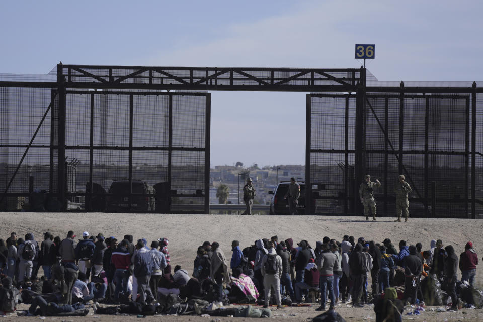 Migrants who crossed the border from Mexico into the U.S. wait next to the U.S. border wall where U.S. Border Patrol agents stand guard, seen from Ciudad Juarez, Mexico, Thursday, March 30, 2023. (AP Photo/Fernando Llano)
