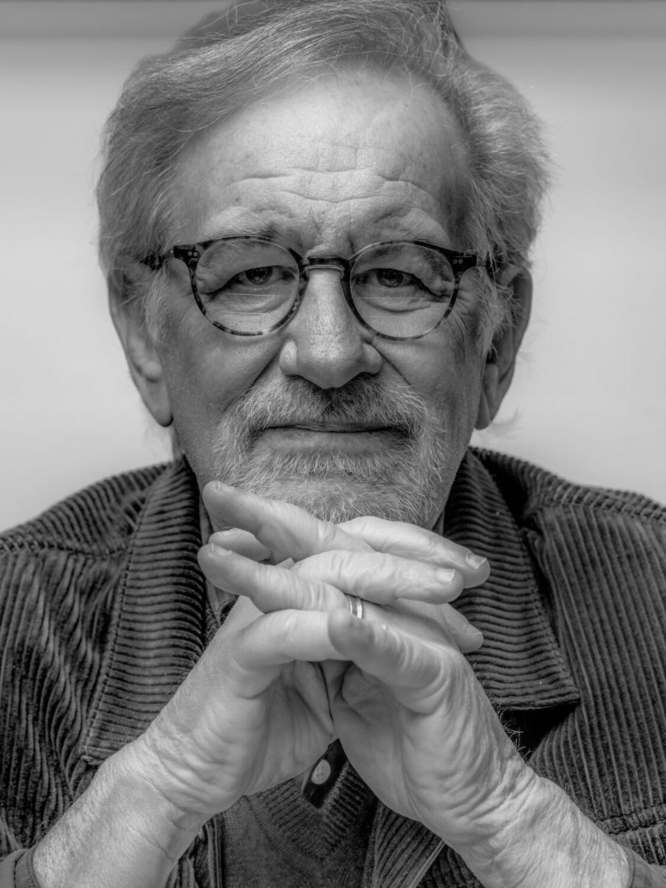 Steven Spielberg folds his hands by his chin for a portrait.