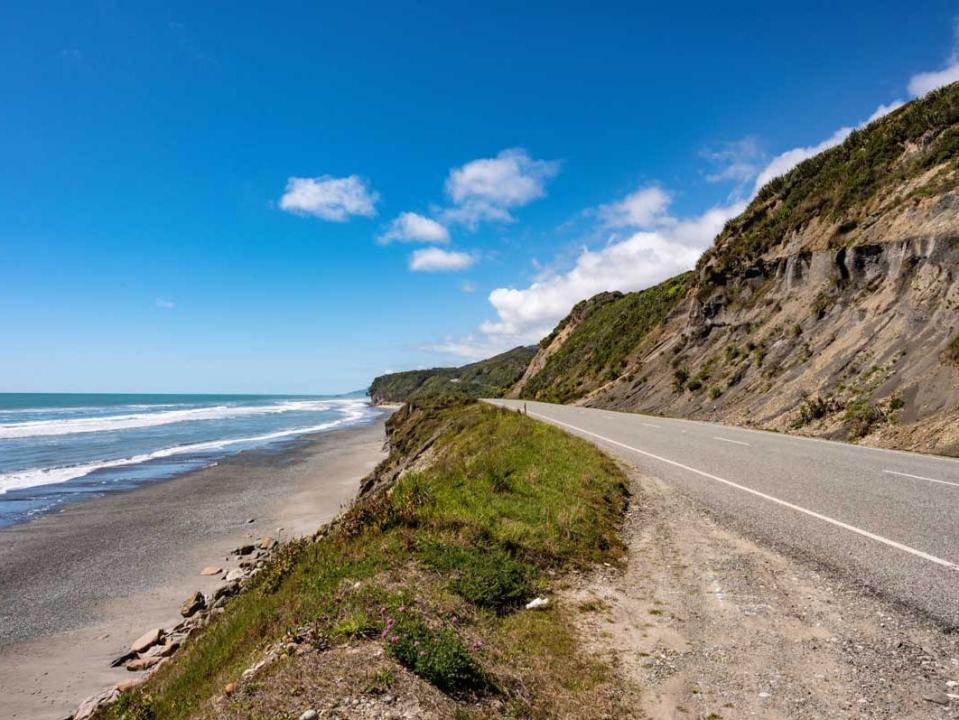 A coastal road with the ocean on one side and hilly green area on the other.